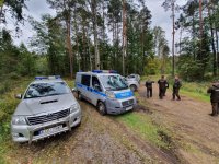 Zdjęcie przedstawia 3 pojazdy Straży Leśnej oraz 1 radiowóz policyjny na drodze leśnej. Na zdjęciu widnieje również pięciu funkcjonariuszy Straży Leśnej.