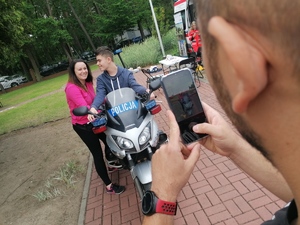 Chłopiec na oznakowanym motorze policyjnym pozuje do zdjęcia z mamą, zdjęcie widać jak wykonuje tata.